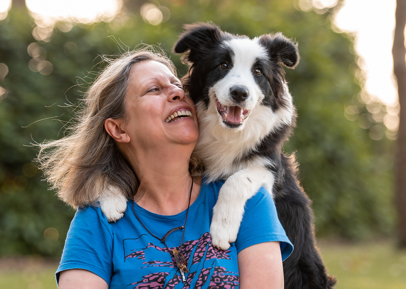 Woman smiling with dog outdoors.