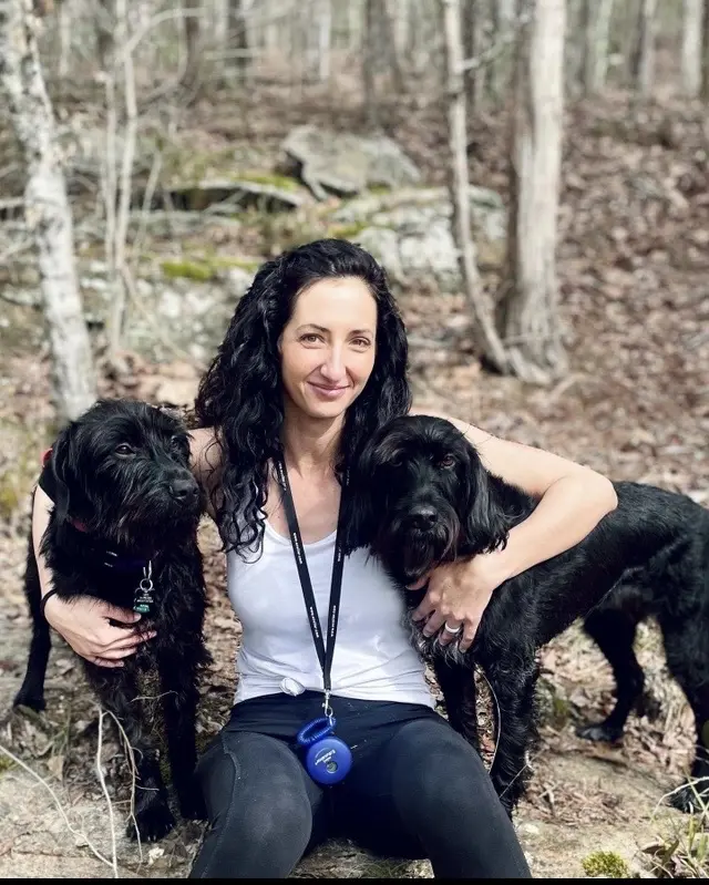 Woman with two black dogs in forest.