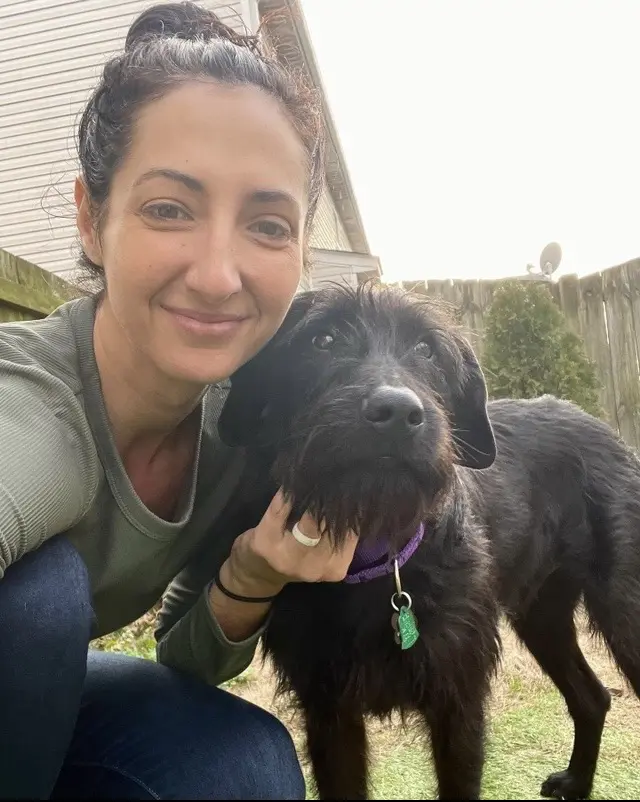 Woman smiling with her black dog outside.