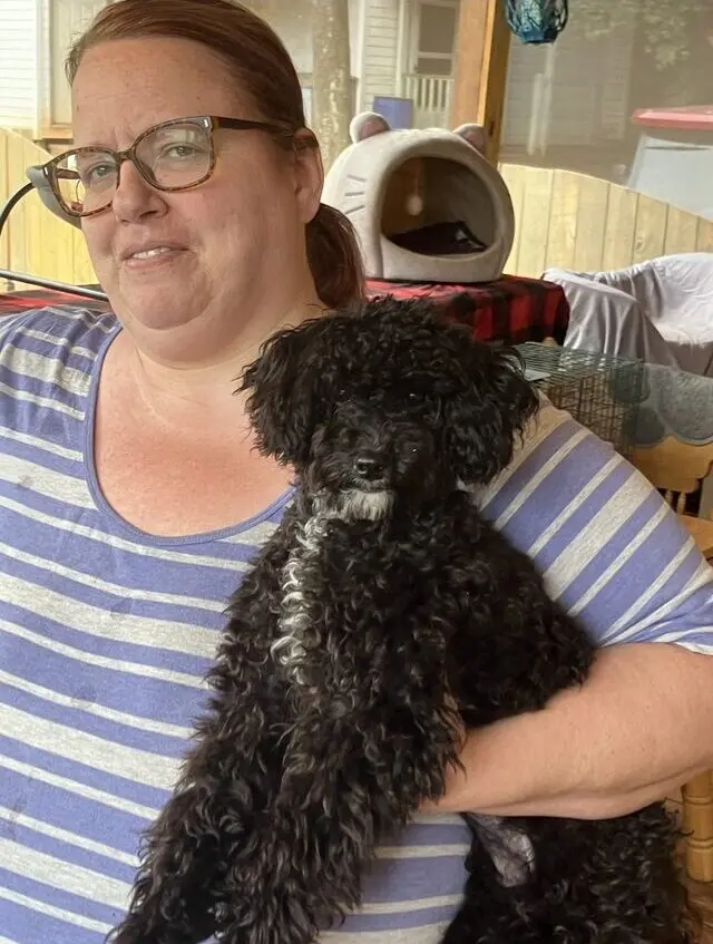 Woman holding a curly-haired black dog.