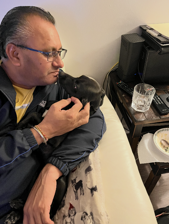 Man affectionately holding a small black puppy.