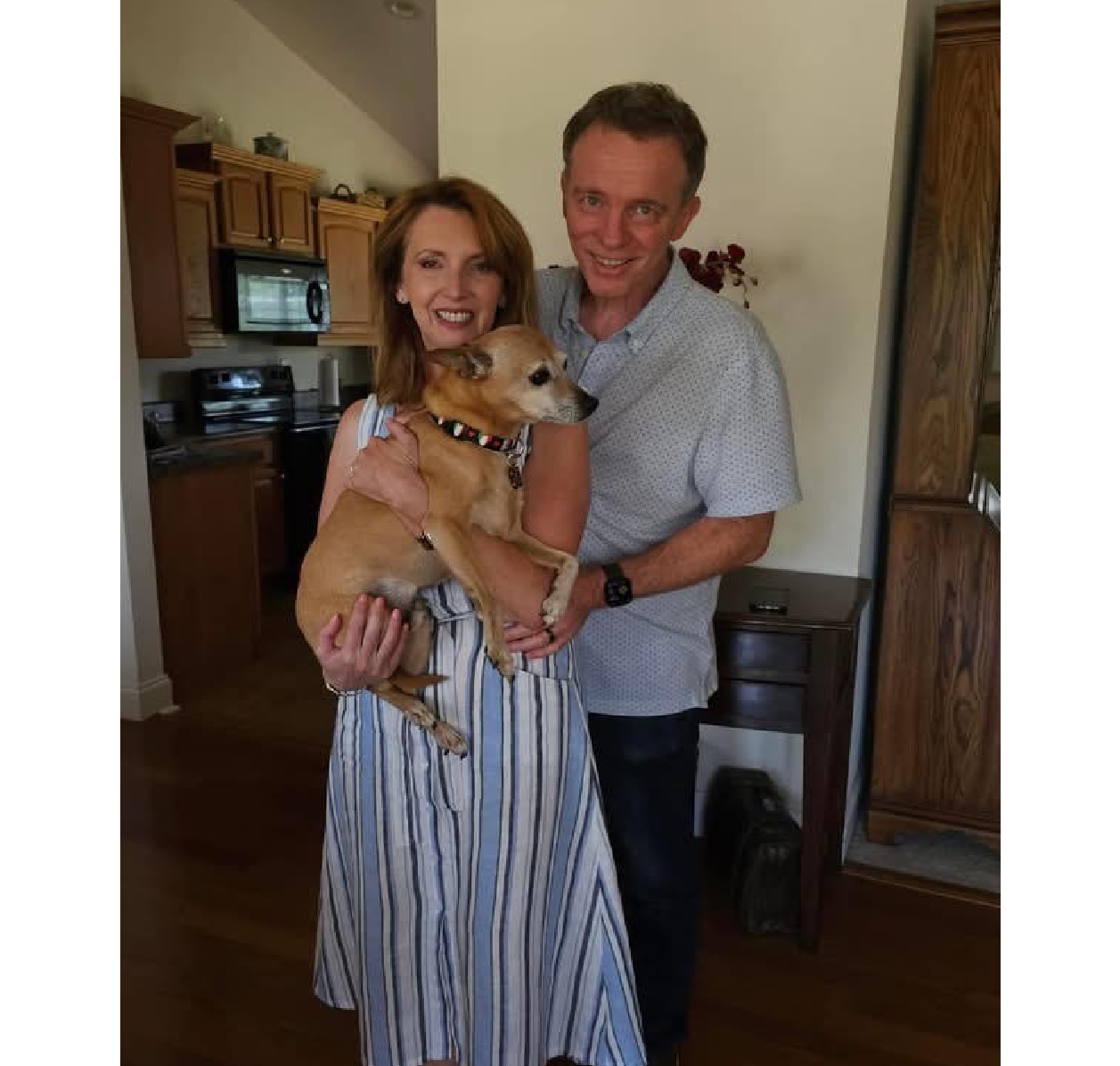 Couple in kitchen holding small tan dog