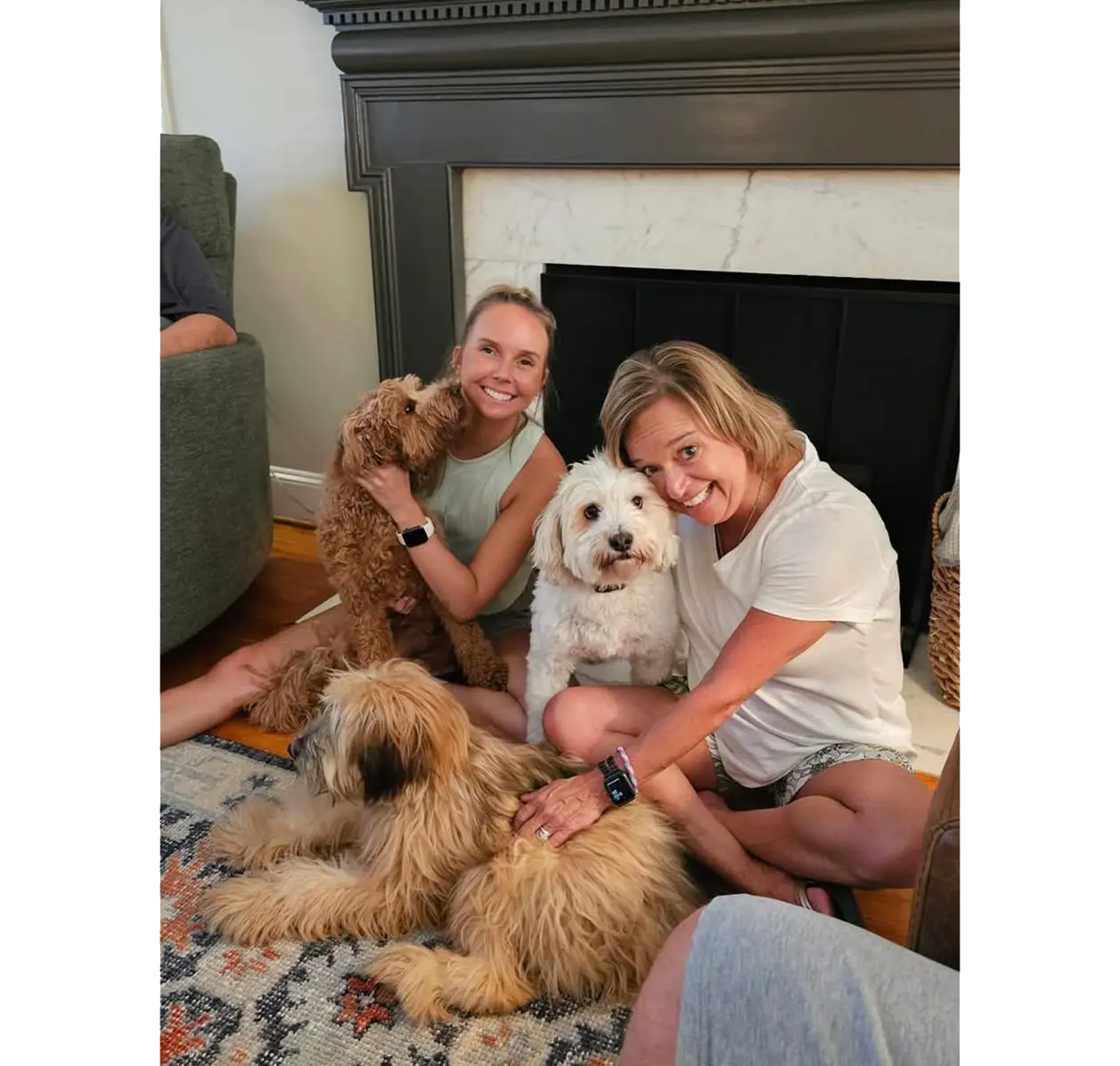 Two women smiling with three dogs by fireplace