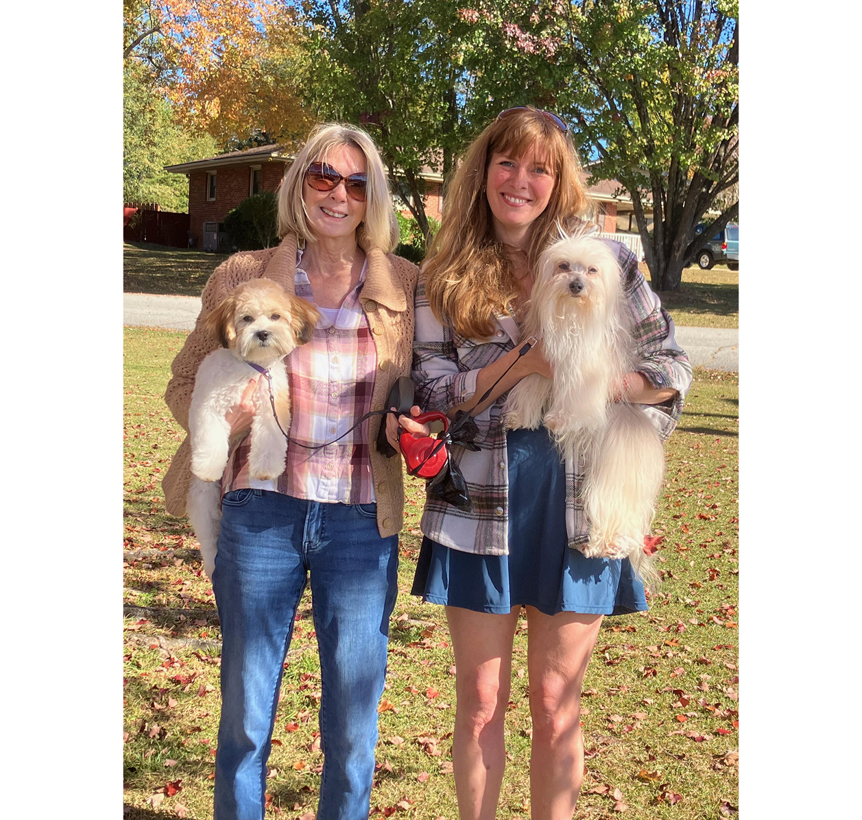 Two women holding small fluffy dogs in autumn