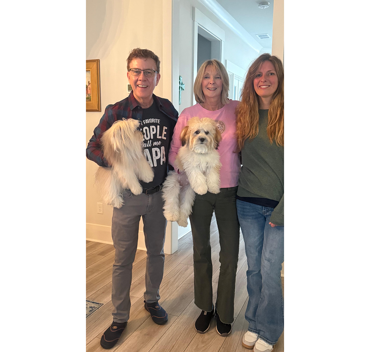 Three smiling people holding two fluffy white dogs