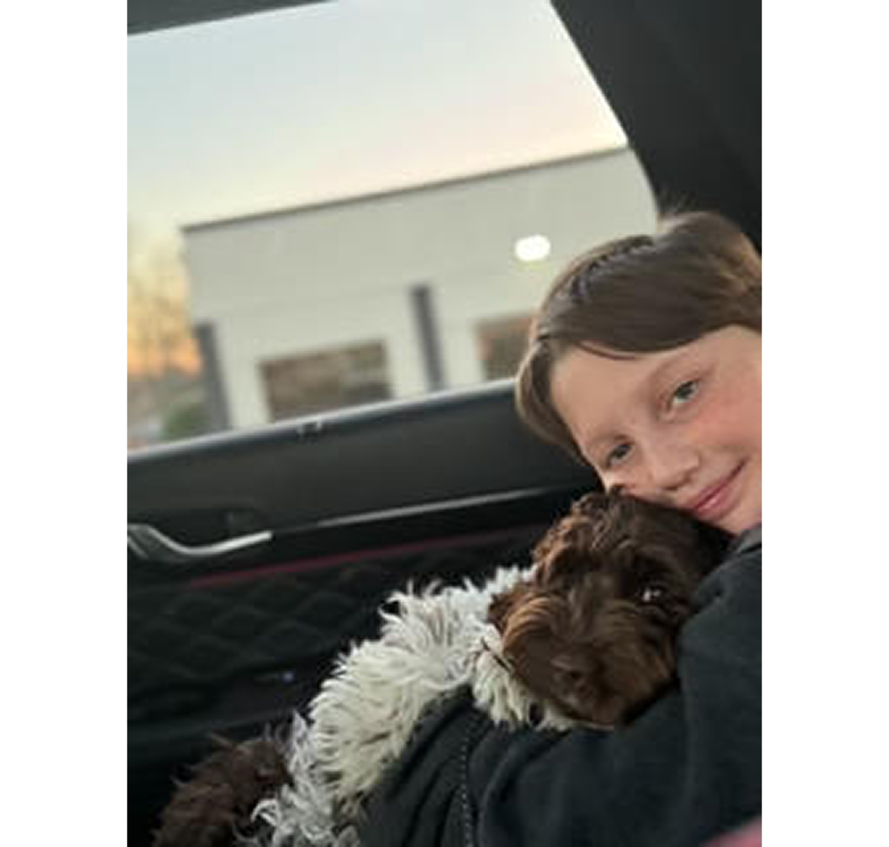 Child cuddling brown-and-white dog in car
